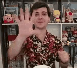 a man in a hawaiian shirt is waving his hand in front of a shelf filled with stuffed animals .