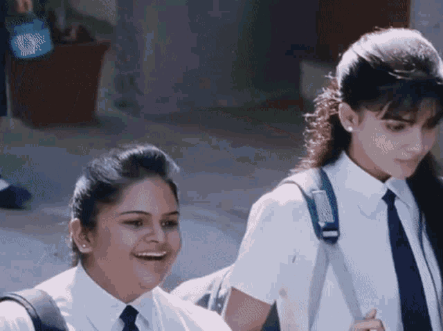 two girls in school uniforms and ties are smiling and laughing
