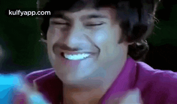 a man in a purple shirt is smiling with his eyes closed and his mouth open .