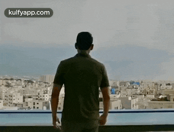 a man is standing on a balcony overlooking a city and a swimming pool .