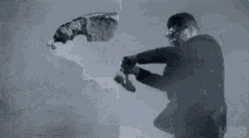 a man in a suit and goggles is holding a hammer and breaking a wall .