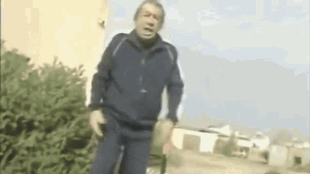 a man in a blue jacket and black pants is standing in a park .