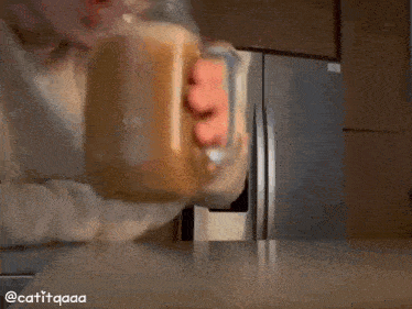 a person is holding a glass mug of coffee in front of a refrigerator