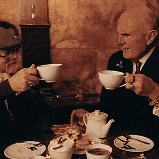 two men sit at a table drinking coffee