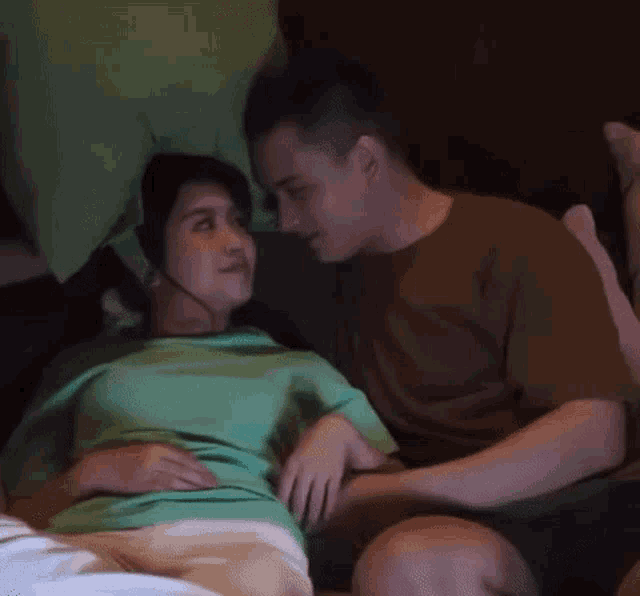 a man and a woman are laying on a bed and the woman is wearing a green shirt