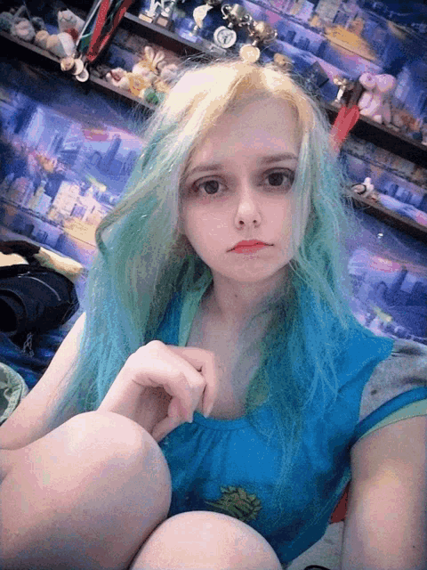 a girl with blue hair is sitting in front of a shelf with trophies on it