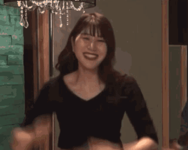 a woman in a black shirt is smiling with her hands up