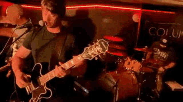 a man is playing a guitar and singing into a microphone while another man plays drums .