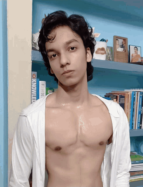 a shirtless young man stands in front of a bookshelf with a book called knowledge on it