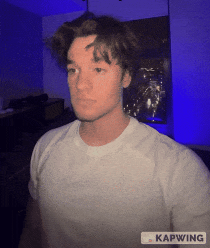 a man in a white t-shirt is standing in front of a blue light and the word kapwing is on the bottom right