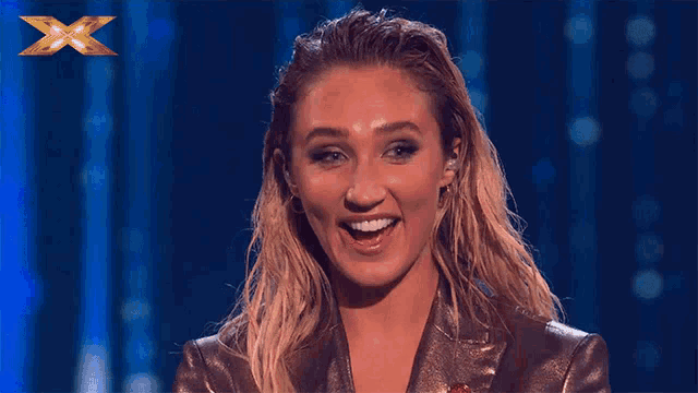 a woman with wet hair is smiling in front of a blue background with a gold x on it