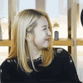 a woman with blonde hair is wearing a black shirt and smiling