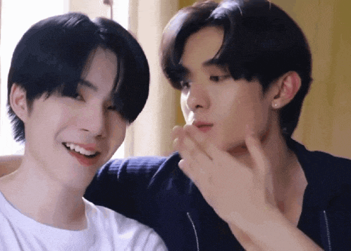 two young men are sitting next to each other and one is touching the face of the other .