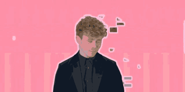a man in a suit stands in front of a pink wall