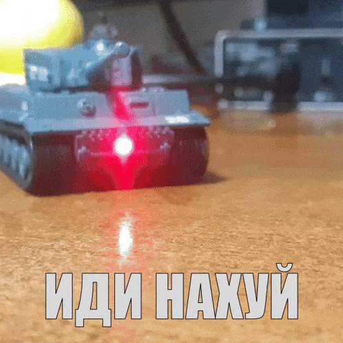 a toy tank is sitting on a wooden table with the words " иди нахуй " in white letters
