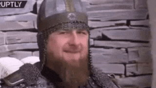 a man with a beard is wearing a helmet and armor and smiling .