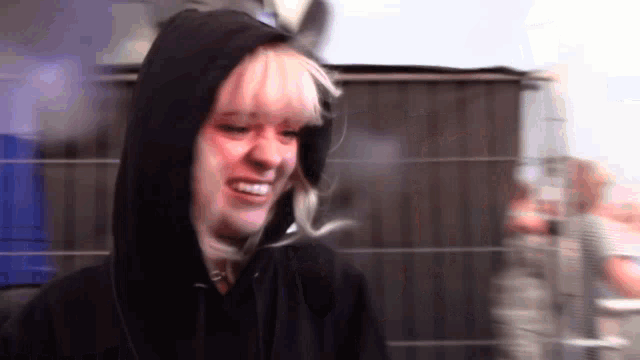 a woman in a black hoodie is smiling and looking at the camera