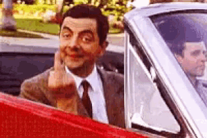a man in a suit and tie is sitting in a car giving the middle finger .