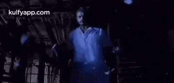a man in a white shirt is standing in a dark room in a dark room .