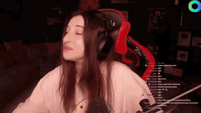 a woman wearing headphones is sitting in a red and black gaming chair with her eyes closed .