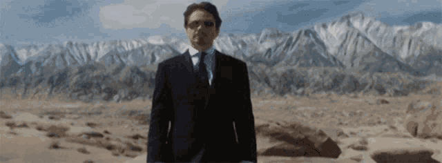 a man in a suit and tie stands in front of a mountain range
