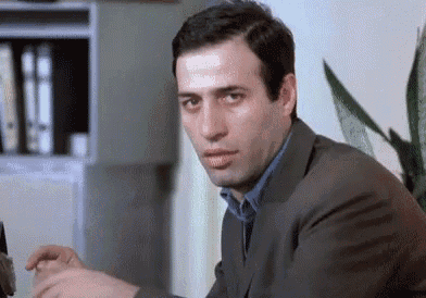 a man in a suit is sitting at a desk in front of a plant .
