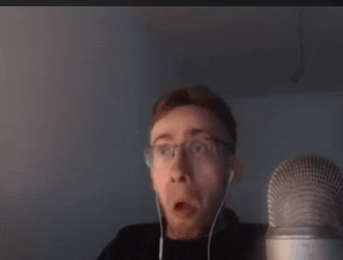 a man wearing glasses and earbuds is sitting in front of a microphone .