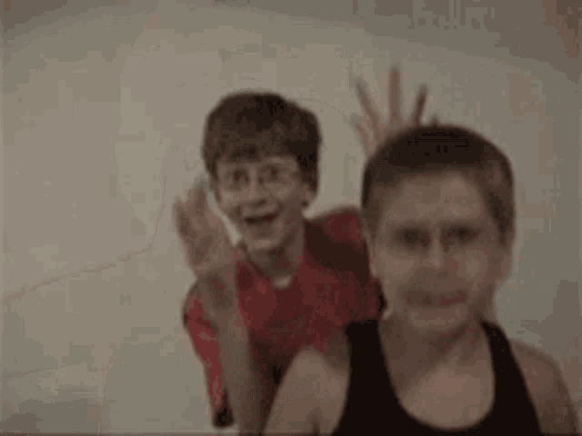 two young boys are standing next to each other and waving .