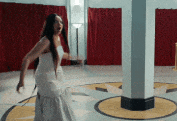 a woman in a white dress is walking in a room with red curtains