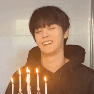 a young man is standing in front of a birthday cake with candles .