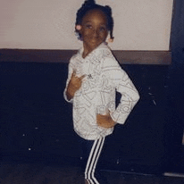 a little girl is standing with her hands on her hips and wearing a white hoodie and black pants .