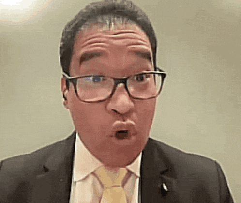 a man in a suit and tie with glasses is making a funny face .
