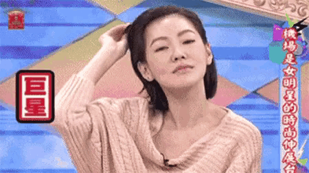 a woman in a sweater is holding her hair in front of a colorful background with chinese writing on it .