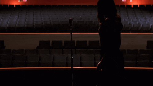 a woman is standing on a stage in an auditorium with empty seats