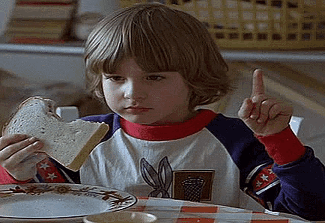a young boy is sitting at a table eating a slice of bread and making a funny face .