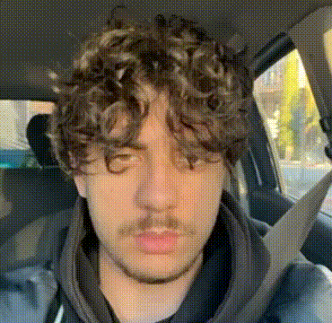 a man with curly hair and a beard is sitting in a car .