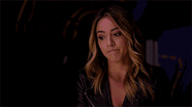 a woman in a leather jacket is sitting in a dark room and looking at the camera .