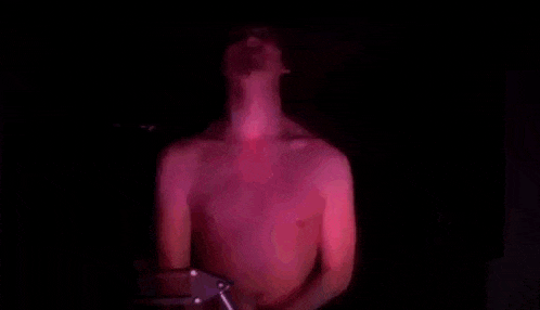 a shirtless man is flexing his muscles in a dark room with a red light behind him .