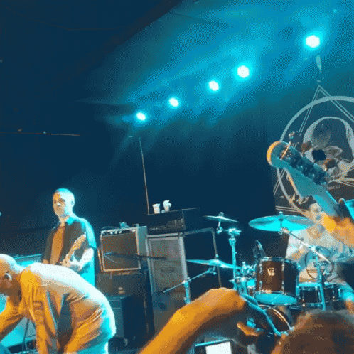a man playing a guitar in front of a drum set with a skull on the wall
