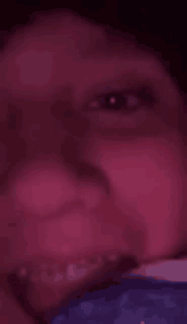 a close up of a person 's face in a dark room with a purple background .