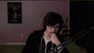 a young man wearing headphones and glasses is playing a guitar in front of a microphone .