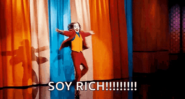 the joker is dancing on a stage in front of a colorful curtain with the words `` soy rich '' written below him .