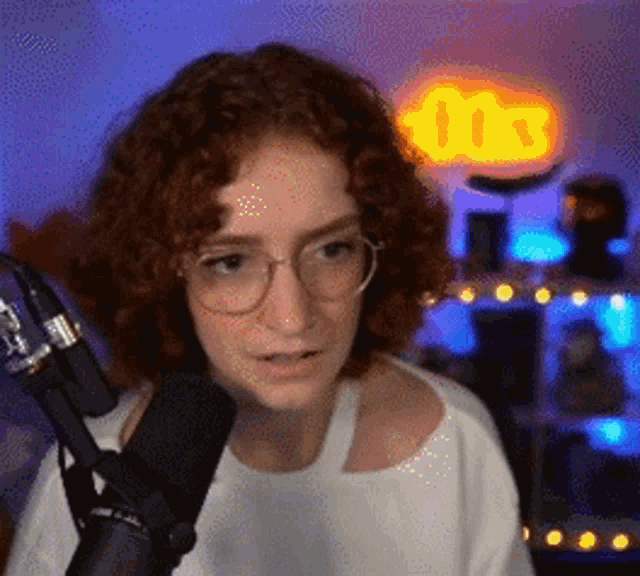 a woman with red hair and glasses is standing in front of a microphone in a room .