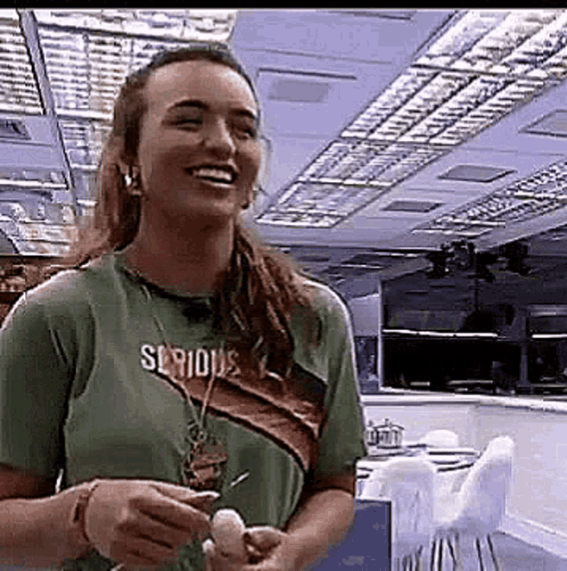 a woman wearing a green t-shirt with the word serious on it is smiling and holding an egg in her hands .