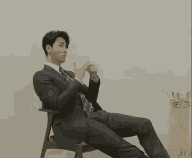 a man in a suit and tie is sitting in a chair with his legs crossed and taking a picture of himself .