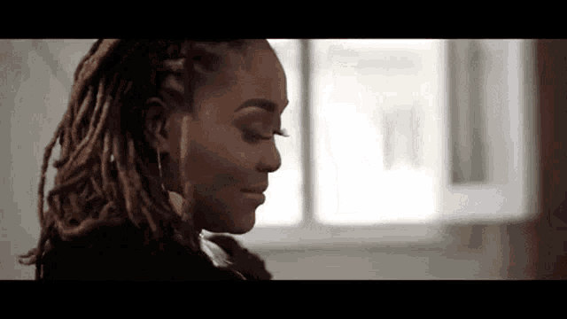 a close up of a woman 's face with dreadlocks looking down .