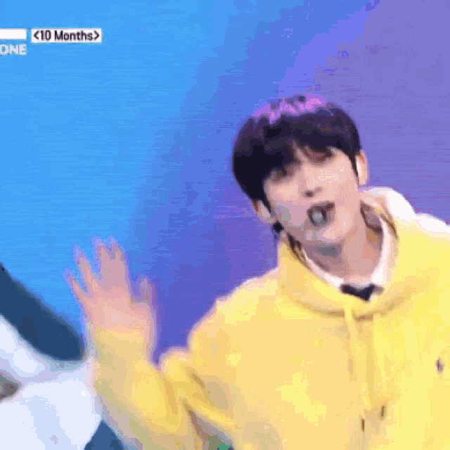 a man in a yellow hoodie is dancing on a stage with his hands in the air .