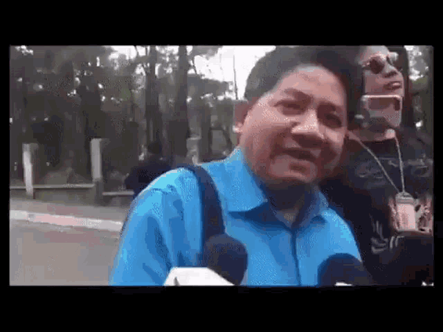 a man in a blue shirt is talking into a microphone while another man takes a picture of him .