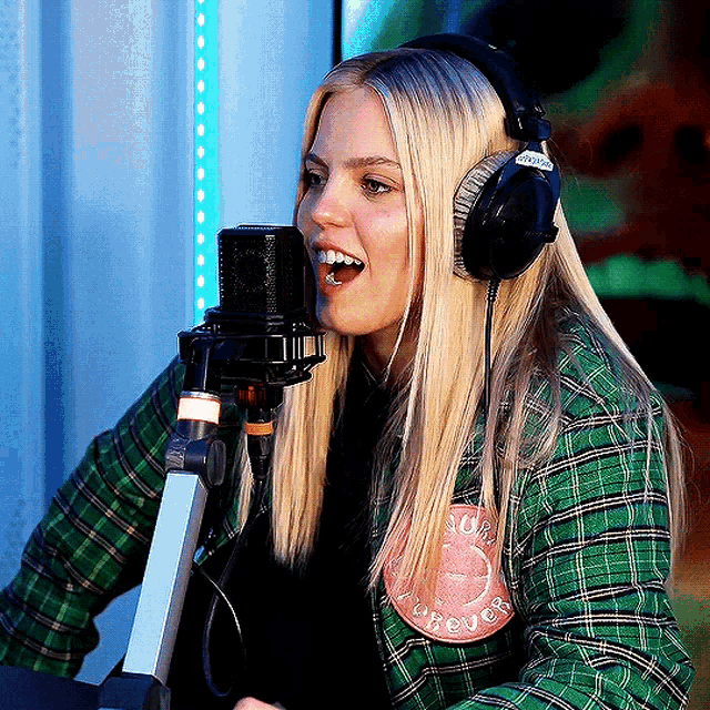 a woman wearing headphones and a green plaid shirt has a patch on her shirt that says forever