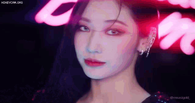 a close up of a woman 's face with a neon sign behind her .